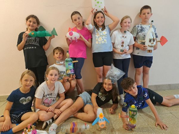 Kinder und Lehrerinnen sitzen vor einer Hüpfburg. Die Sonne scheint. 