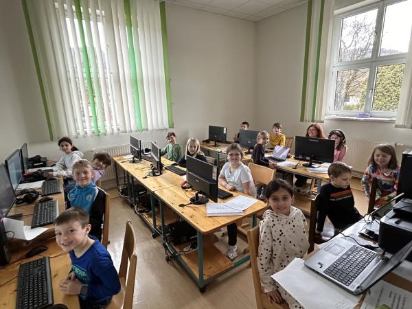 die Kinder der 2. Klassen lachen in die Kamera und arbeiten an PCs