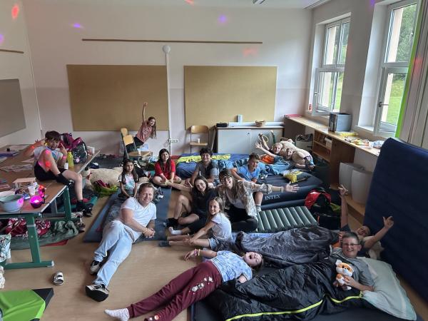 Kinder und Lehrer:innen liegen in der Klasse und lachen