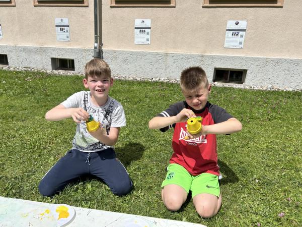 Zwei Burschen bemalen Tontöpfe in gelb und sitzen auf der Wiese 