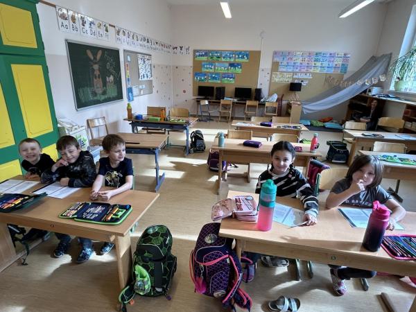 Kinder sitzen in der ersten Tischreihe und lesen einen Text 